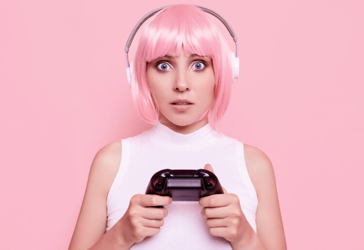 Portrait of gorgeous happy sexy gamer girl with pink hair playing video games using joystick on colorful background in studio